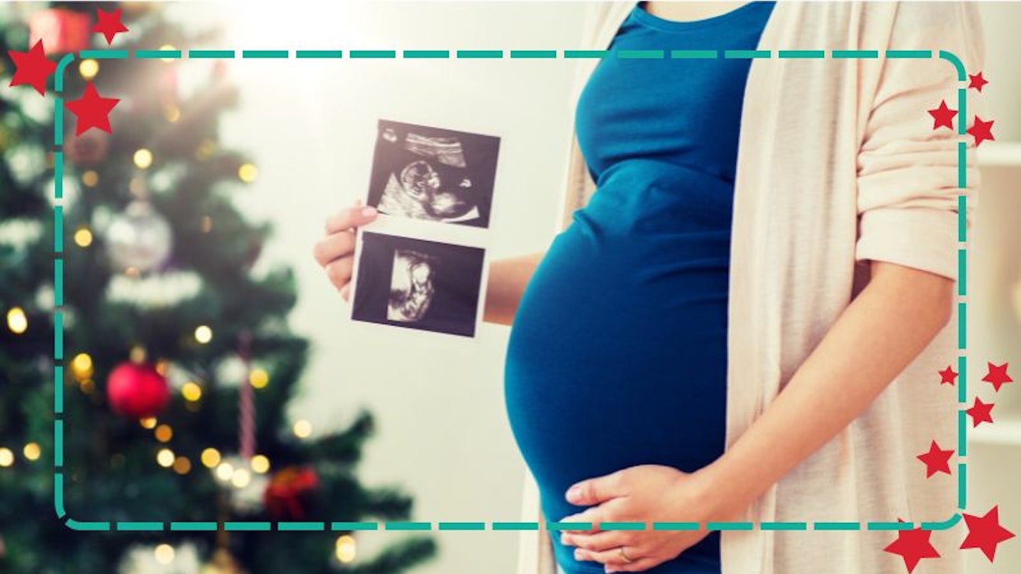 A woman pregnant at Christmas and standing in front of a christmas tree, holding a baby scan photo