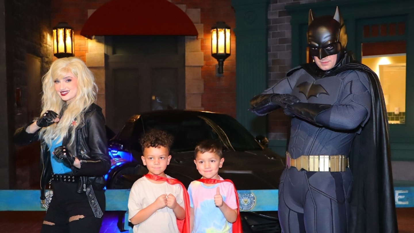 Two boys posing with Batman at Warner Bros. World Yas Island smiling at the camera.