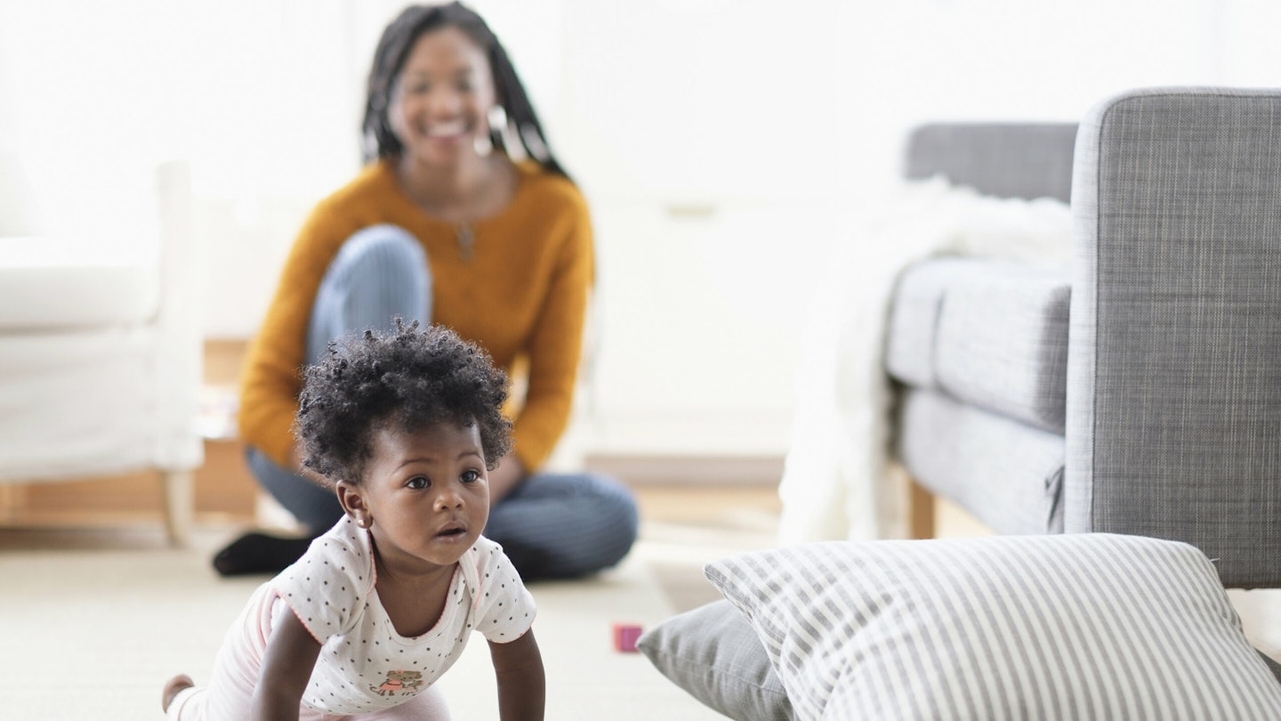 Woman watching baby daughter reach baby milestone development crawl toward pillow