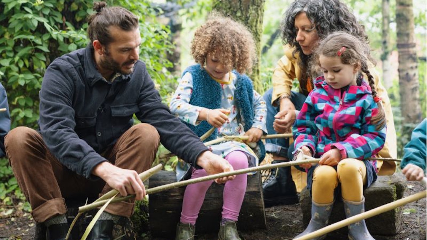 Forest School leader shows children and parent whittling sticks - stock photo Two young girls and Mum learning how to whittle sticks at forest school