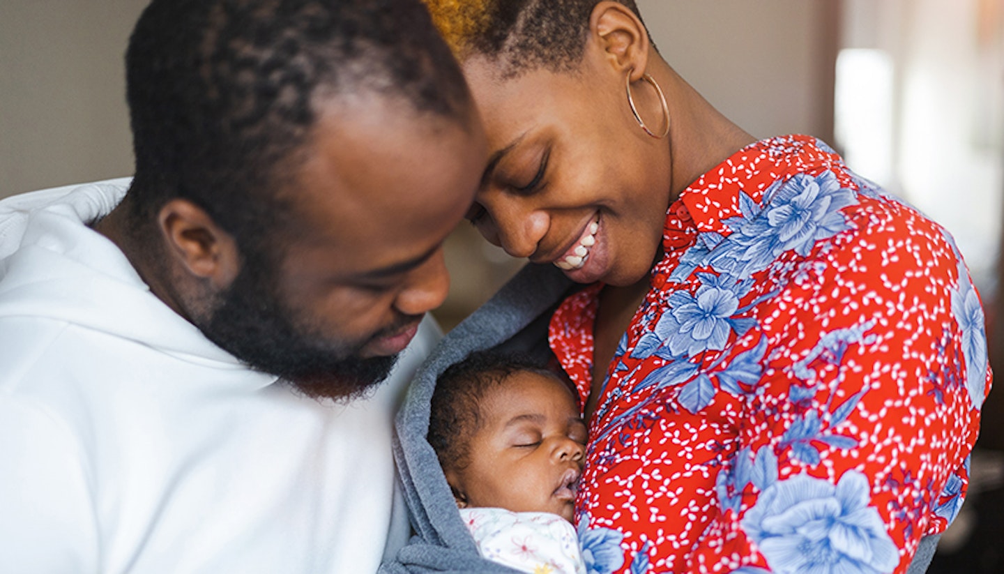 A mother and father cuddling and singing to their baby. The picture displays that love and affection they have for their baby.