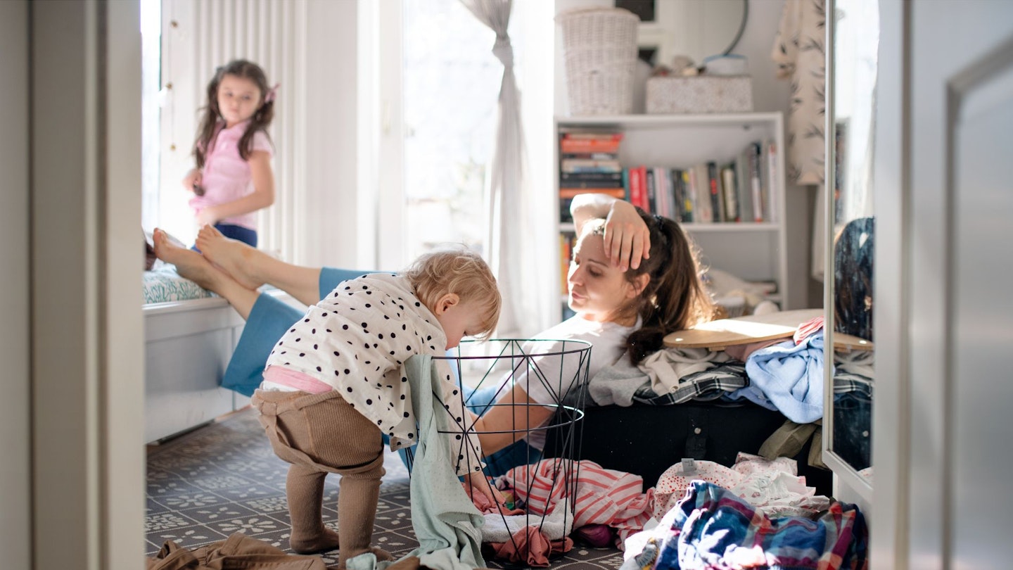Tired Mother with Small Toddler Daughter in Messy Bedroom at Home, Resting.