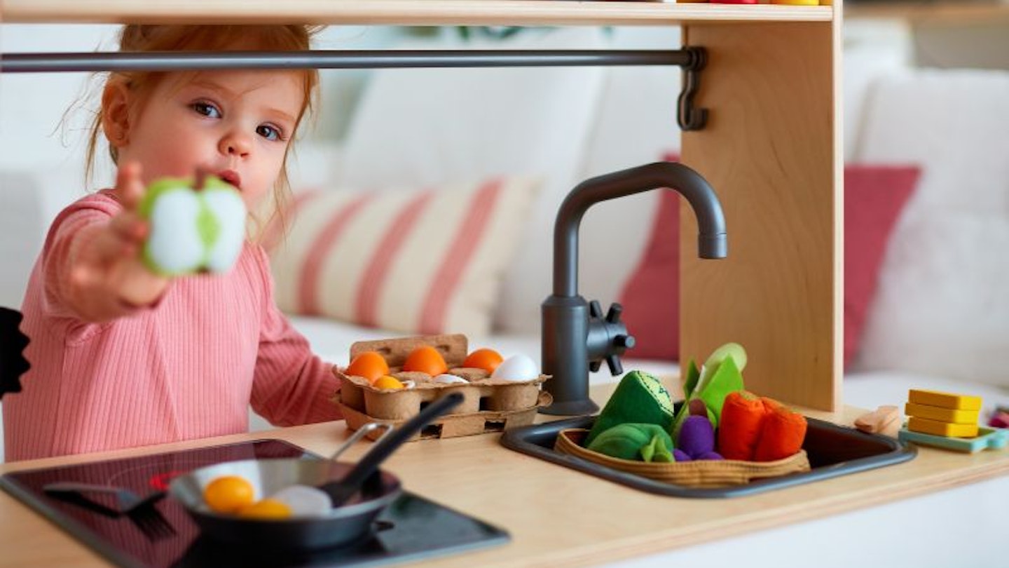 Toddler holding a toy apple and playing with toy food in a play kitchen