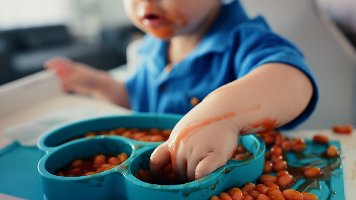 Baby, hands and mess in chair with food for mealtime or appetite, self feeding and learning to eat with sensory experience. Boy toddler, beans and growth development or milestone and nutrition.