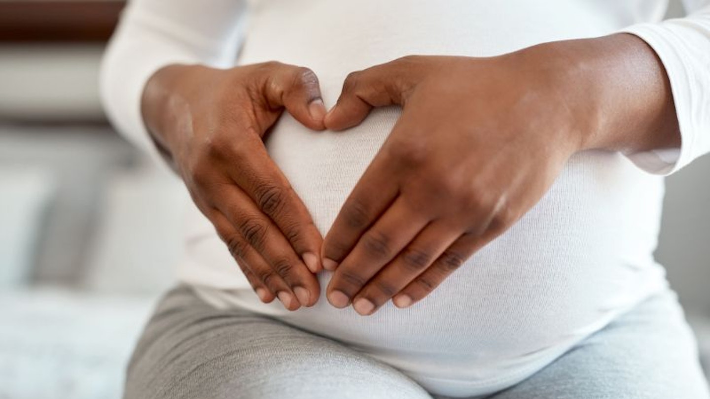 Woman holding her pregnant bump and making a heart shape with her hands