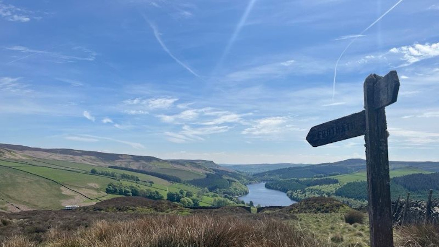 Blue sky, hills and a valley with a lake at the bottom, and a signpost in the foreground