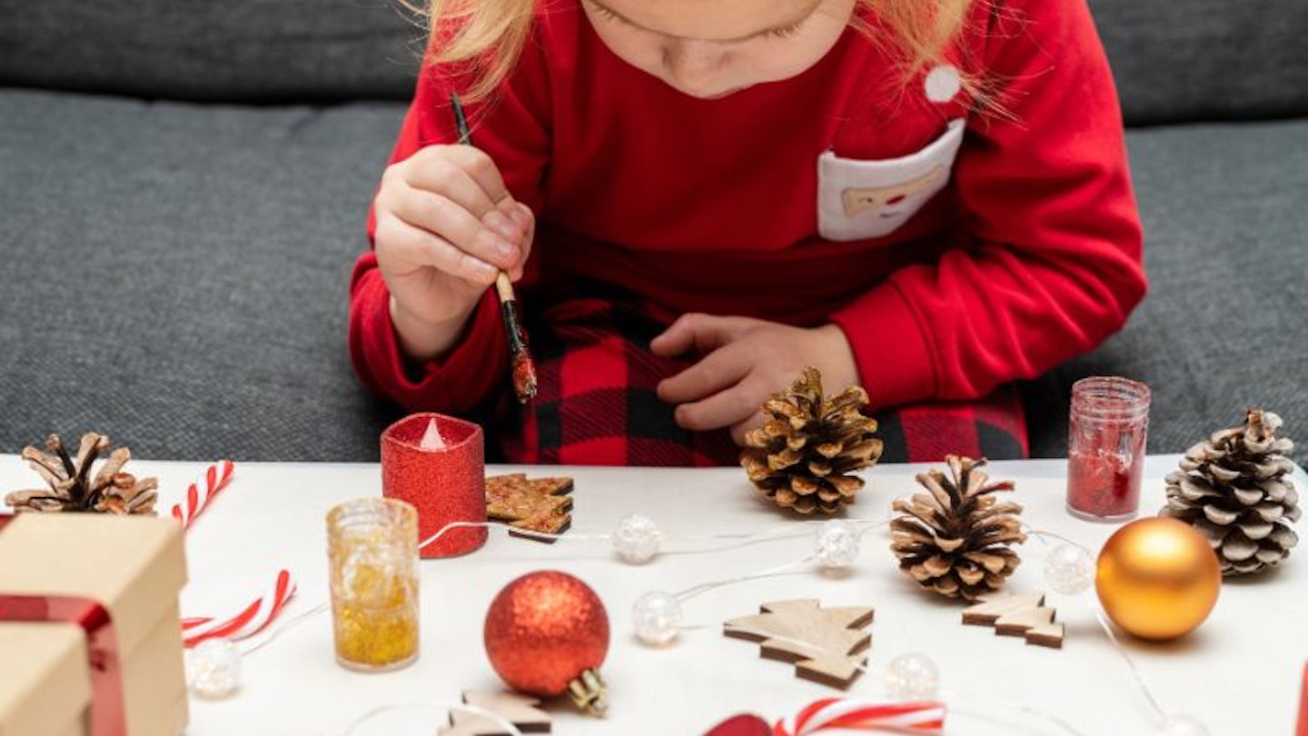 A little girl in a red dress concentrating on toddler Christmas crafts