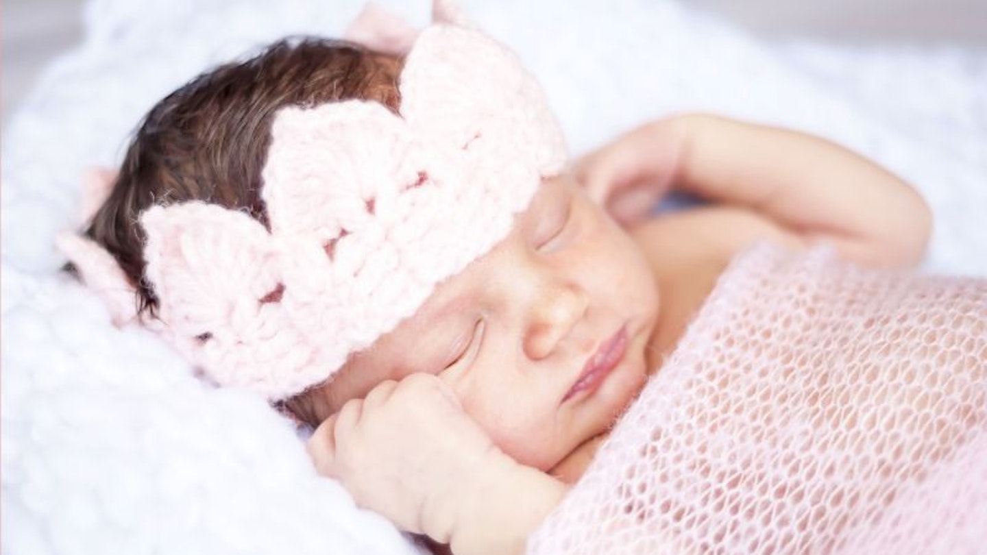 A baby girl sleeping in a pink blanket with a pink knitted crown on her head